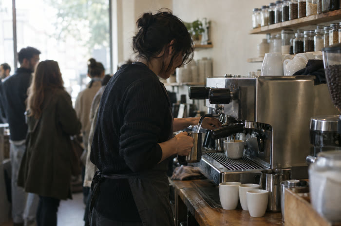 A coffee shop owner steaming milk during the morning rush.